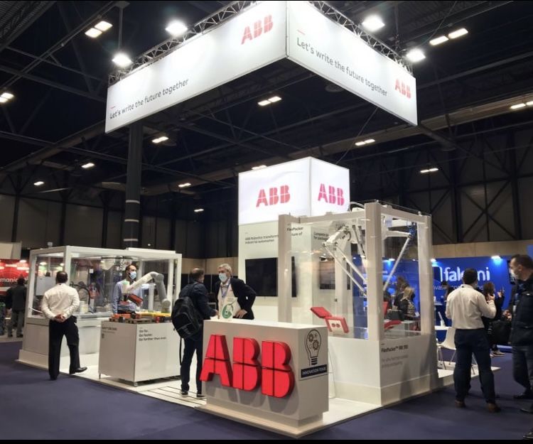 Stand de ABB en una feria tecnológica, con visitantes observando demostraciones de robótica y automatización industrial.