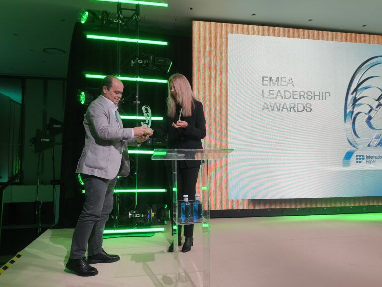 Un hombre entrega un premio a una mujer en el escenario durante los EMEA Leadership Awards, con un fondo de pantalla que muestra el título del evento y el logotipo de International Paper