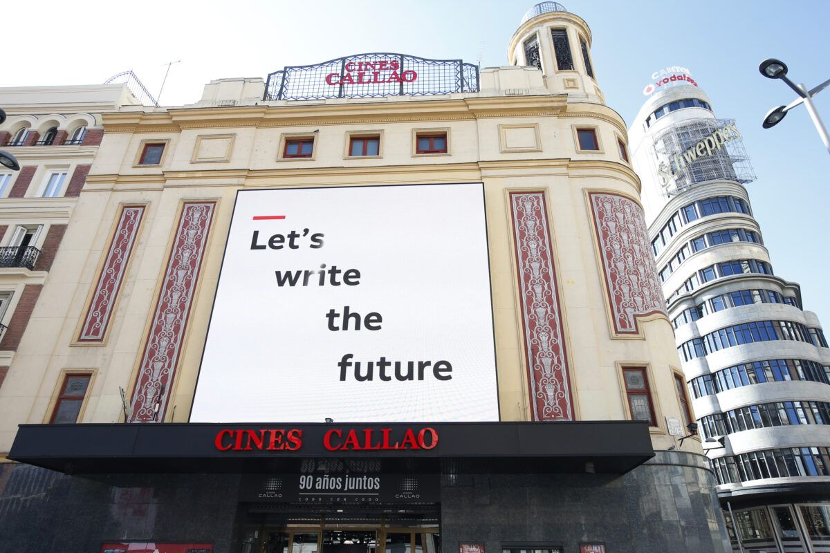Fachada exterior del edificio Cines Callao en Madrid en un día soleado. Una gran pantalla digital en la fachada muestra el texto "Let's write the future". A la derecha se ve el icónico edificio con el cartel luminoso de Schweppes.