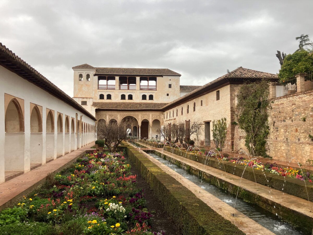 Vista de un jardín con fuentes, flores y arcos en estilo andalusí dentro de un conjunto monumental histórico. En la Alhambra de Granada.