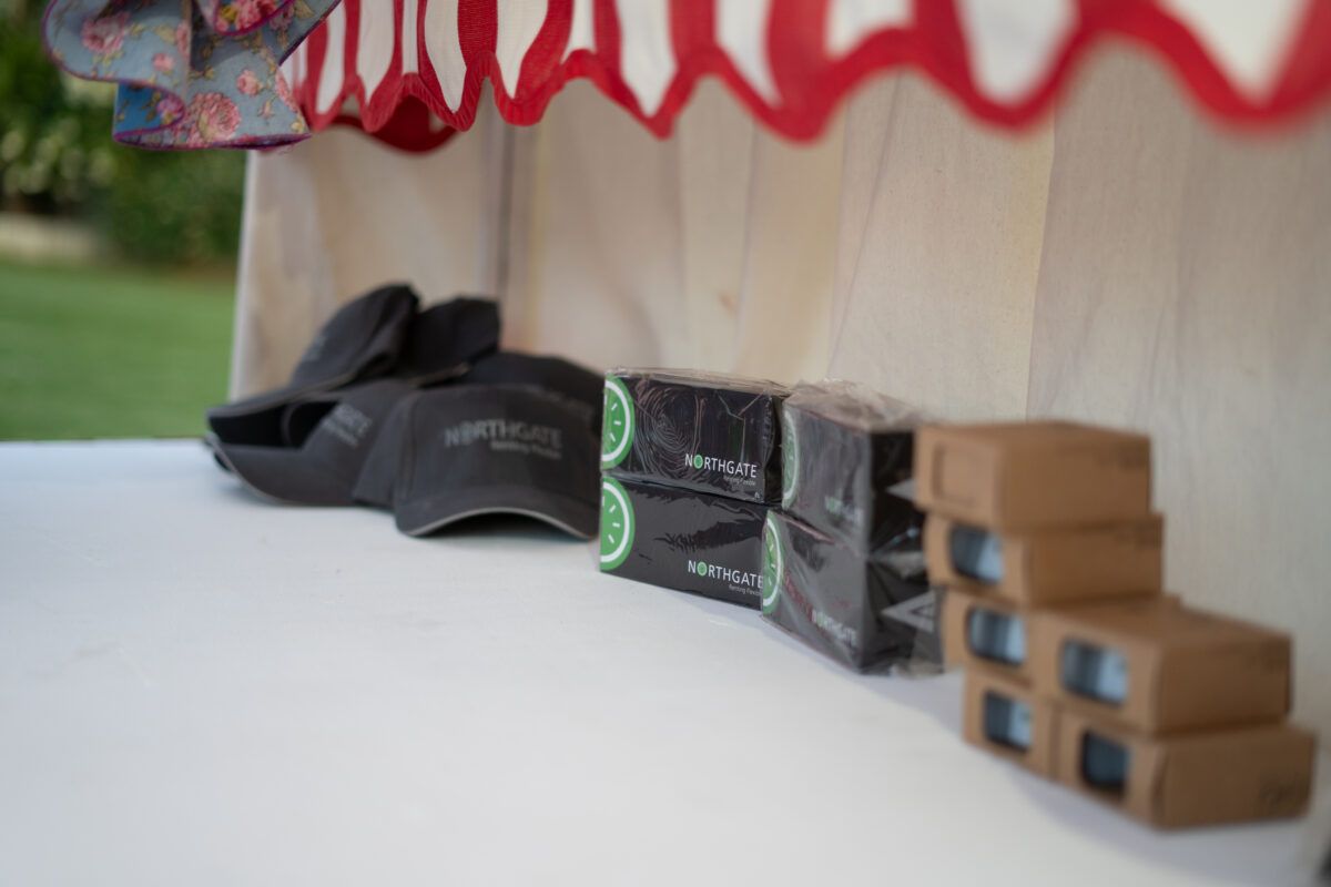 Artículos promocionales de la marca Northgate, incluyendo gorras y pequeñas cajas negras con el logotipo de la empresa, expuestos sobre una mesa en un evento.