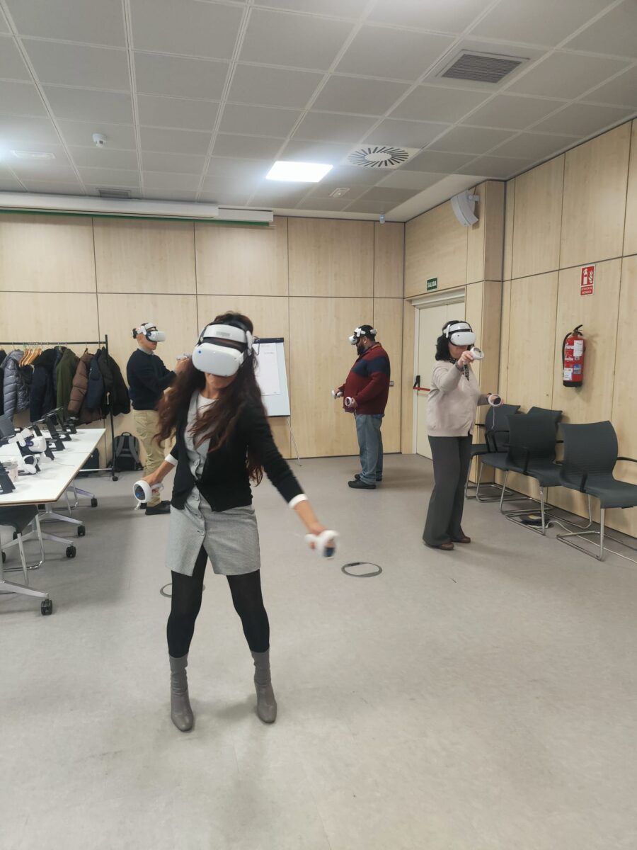 Cuatro personas con auriculares de realidad virtual blancos y controladores, participando en una sesión de entrenamiento o actividad de grupo en una sala de oficina.
