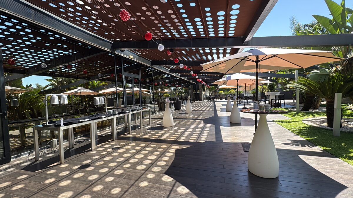 Terraza exterior moderna y sombreada con mesas altas tipo cóctel y zonas de buffet preparadas para un evento.
