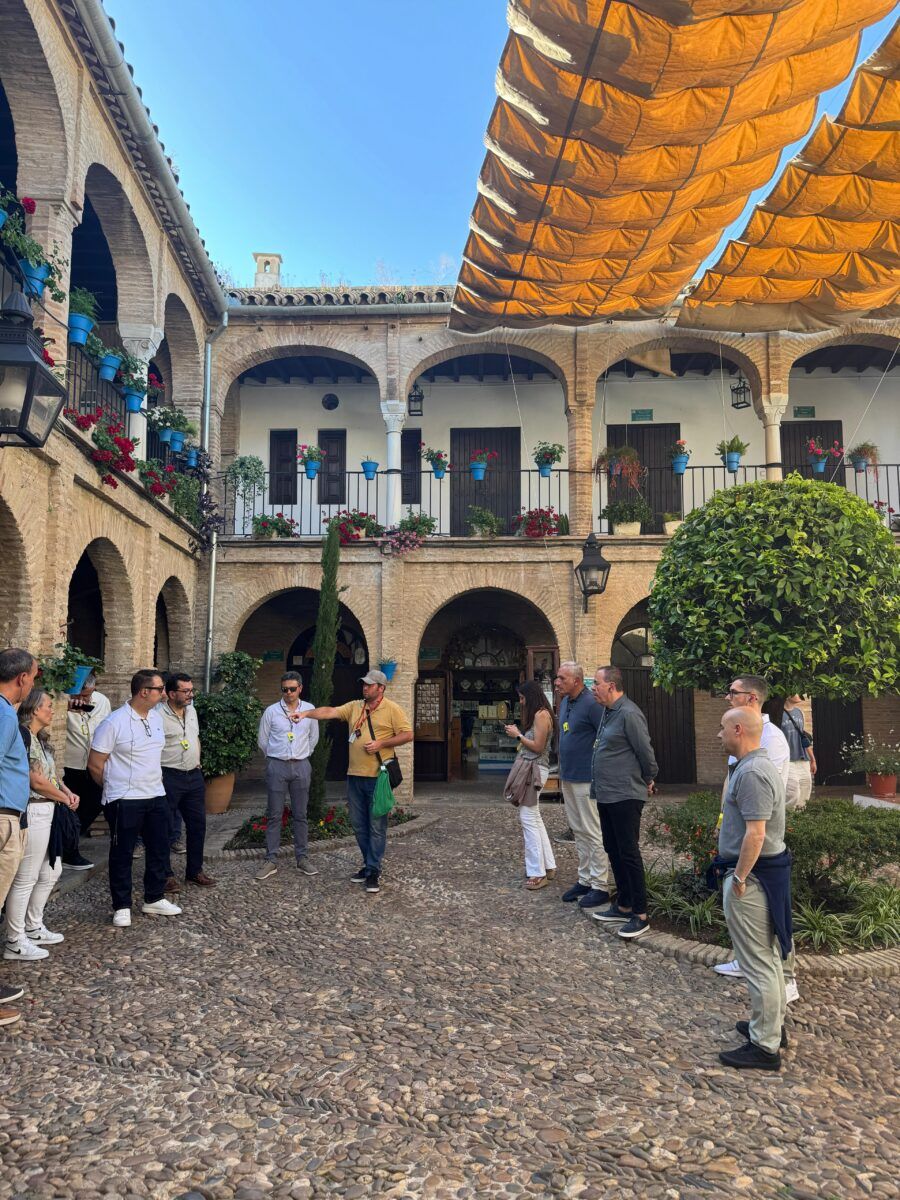 Grupo de personas atendiendo a una explicación de un guía turístico en un patio tradicional andaluz con macetas azules y flores en los balcones.