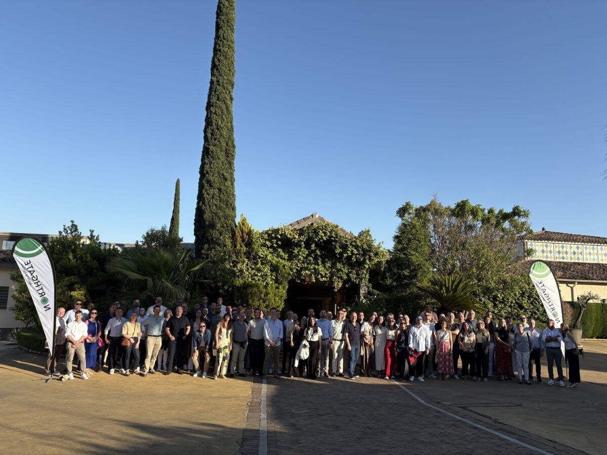 Foto de grupo de los invitados a la convención posando en la entrada ajardinada de una finca con banderas publicitarias de Northgate.