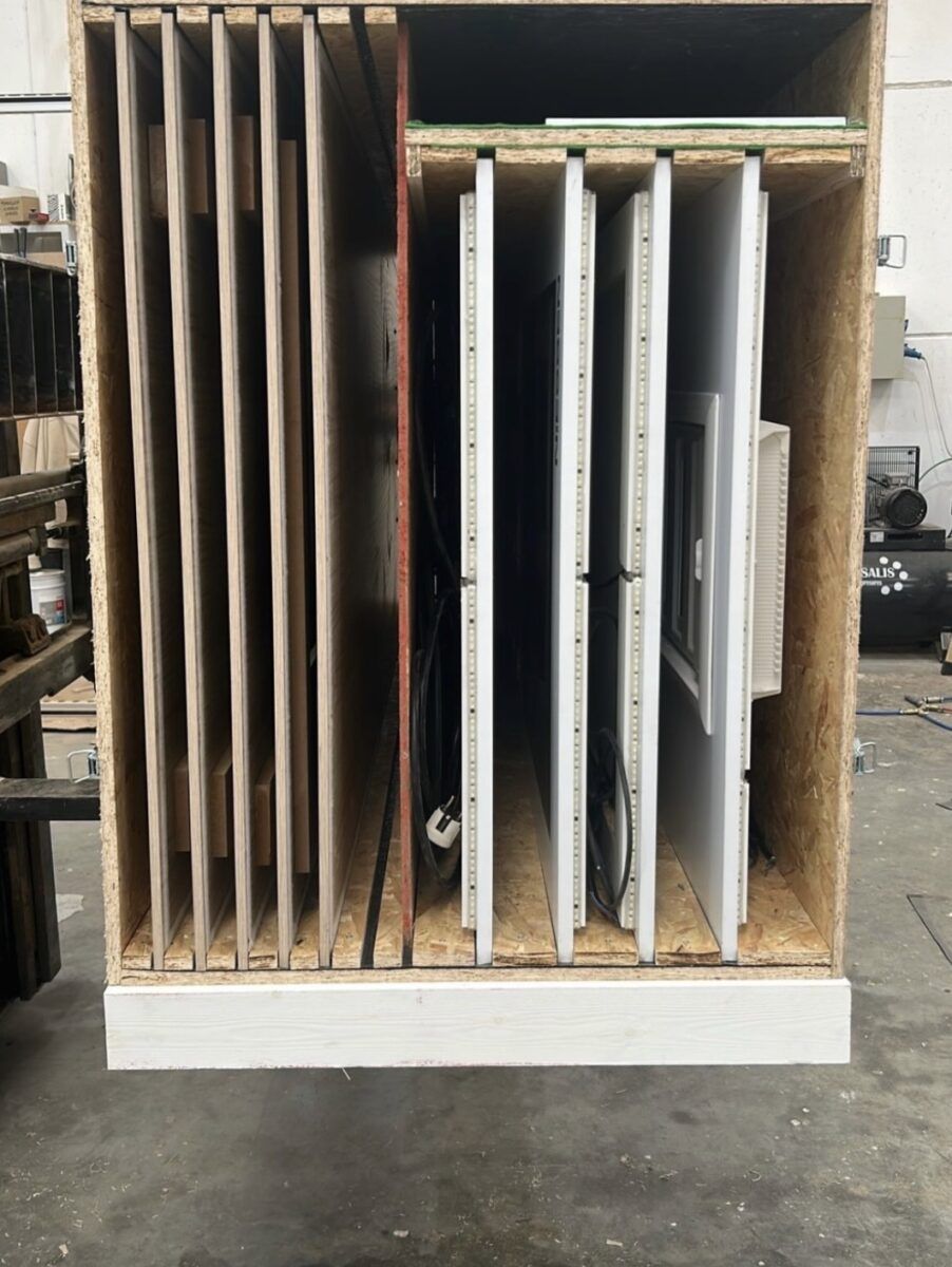 Caja de embalaje técnica o contenedor de transporte fabricado en madera OSB con divisiones verticales internas, cargado con paneles de madera y expositores de productos eléctricos cableados.